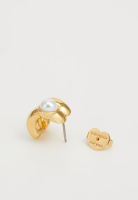Gold-tone metal stud earring featuring a pearl centerpiece, flower-shaped design, and a heart-shaped backing with engraved branding.