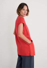 Rode linnen tuniek met korte mouwen en zijzakken, met een losse pasvorm en zijsplitten, gecombineerd met marineblauwe wijde broek.