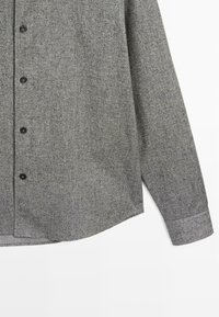 Camicia grigia con bottoni, realizzata in un tessuto textured, con colletto a punta, bottoni neri e orlo curvo. Maniche lunghe con polsini abbottonati.