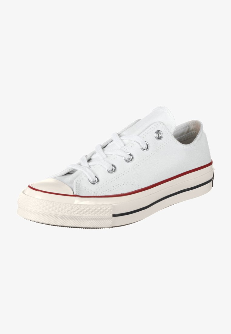 White canvas sneaker with a low profile, rubber toe cap, and classic red and black striped midsole. Features metal eyelets and laces.