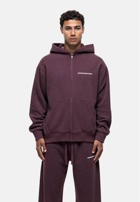 Paarse zip-up hoodie van zachte stof, met een voorzak en een opvallend "GOODFORNOTHING" logo op de linkerborst. Bijpassende sweatpants.