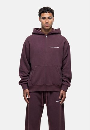 Purple zip-up hoodie made of soft fabric, featuring a front pocket and bold "GOODFORNOTHING" logo on the left chest. Matching sweatpants.