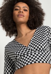 Top cropped xadrez preto e branco com mangas longas e decote em V, feito de um material macio e elástico.