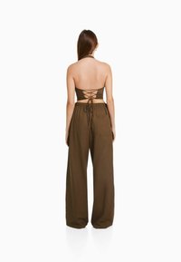 Haut en halter marron avec des détails de dos lacé, associé à un pantalon marron ample et taille haute. Le matériau semble léger et texturé.