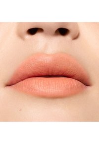 Couleur de lèvres pêche douce avec une finition mate, présentant une texture lisse et une forme naturelle, encadrée par une peau légèrement teintée autour de la bouche.