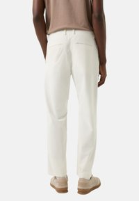 Białe bawełniane spodnie o luźnym kroju, z tylnymi kieszeniami, czystym paskiem w talii, zestawione z jasnymi trampkami.