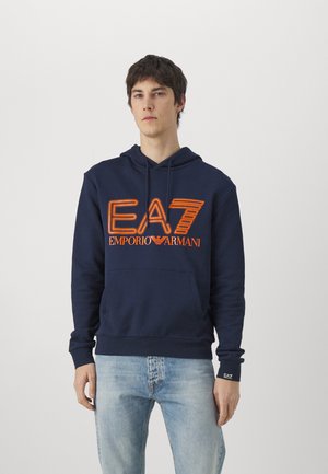 Felpa navy in cotone, con tasca a marsupio, stringhe e logo arancione "EA7 Emporio Armani" stampato sul petto. Vestibilità standard.