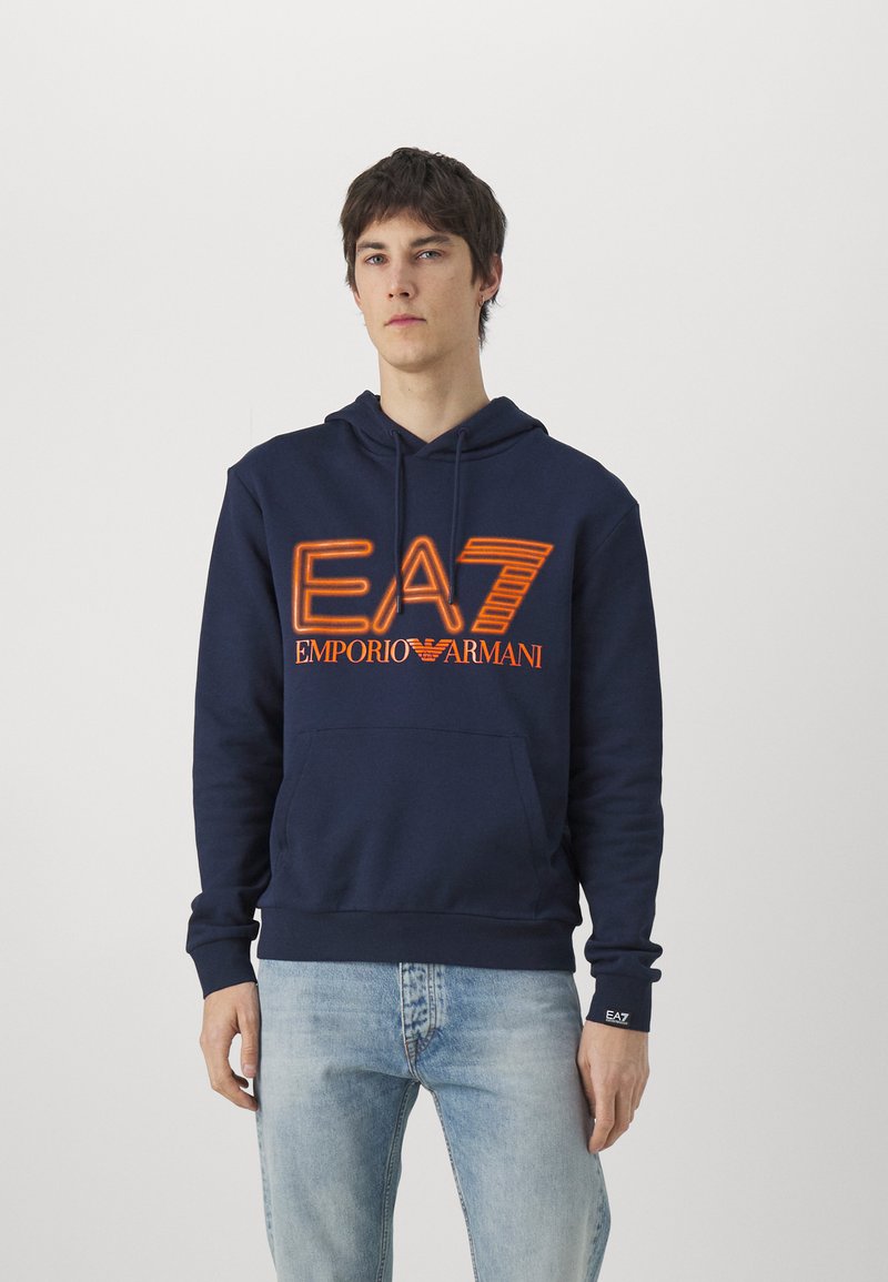 Felpa navy in cotone, con tasca a marsupio, stringhe e logo arancione "EA7 Emporio Armani" stampato sul petto. Vestibilità standard.