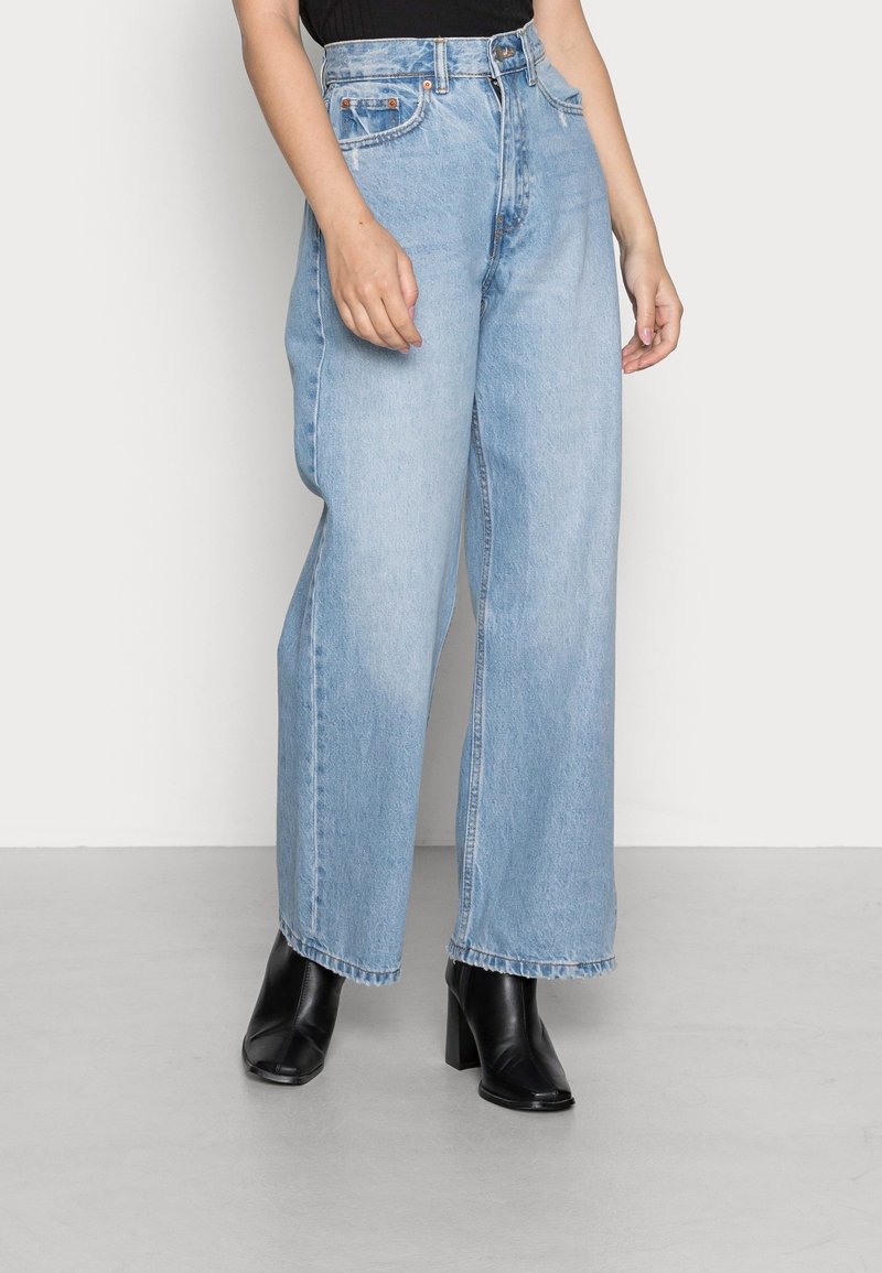 Ljusblå hög midja vida jeans i denim, med fem fickor, synlig sömnad och rå fåll. Matchas med svarta klackstövlar.