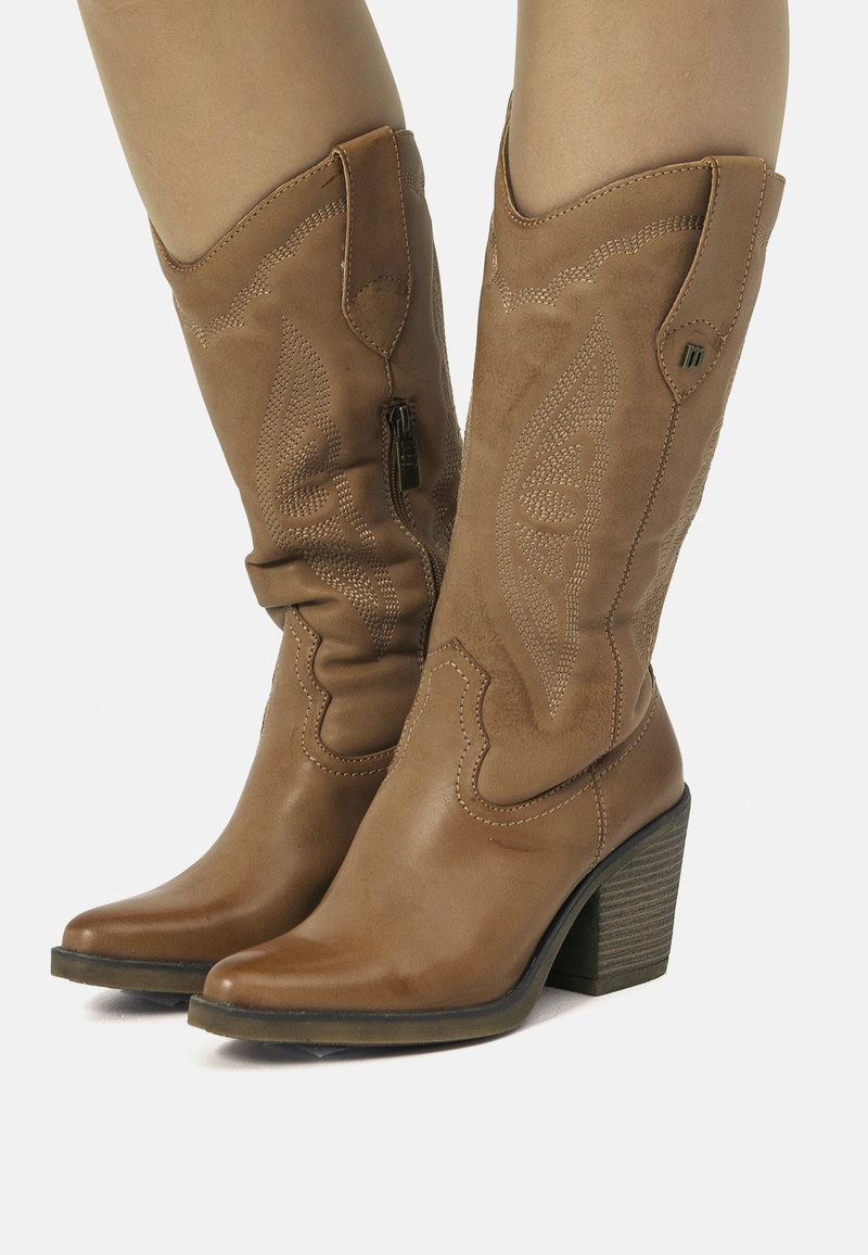 Stivali da cowboy in pelle marrone con punte appuntite, cuciture decorative e tacco impilato. Presentano una cerniera laterale per indossarli facilmente.
