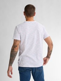 Tricou alb cu dungi subțiri orizontale de diferite culori, mâneci scurte, guler rotund și o croială relaxată. Asortat cu blugi bleumarin.