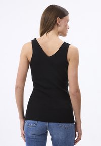 Top da donna nero a coste con scollatura a V e dettagli sulle spalle. Design aderente, abbinato a jeans di denim azzurri.