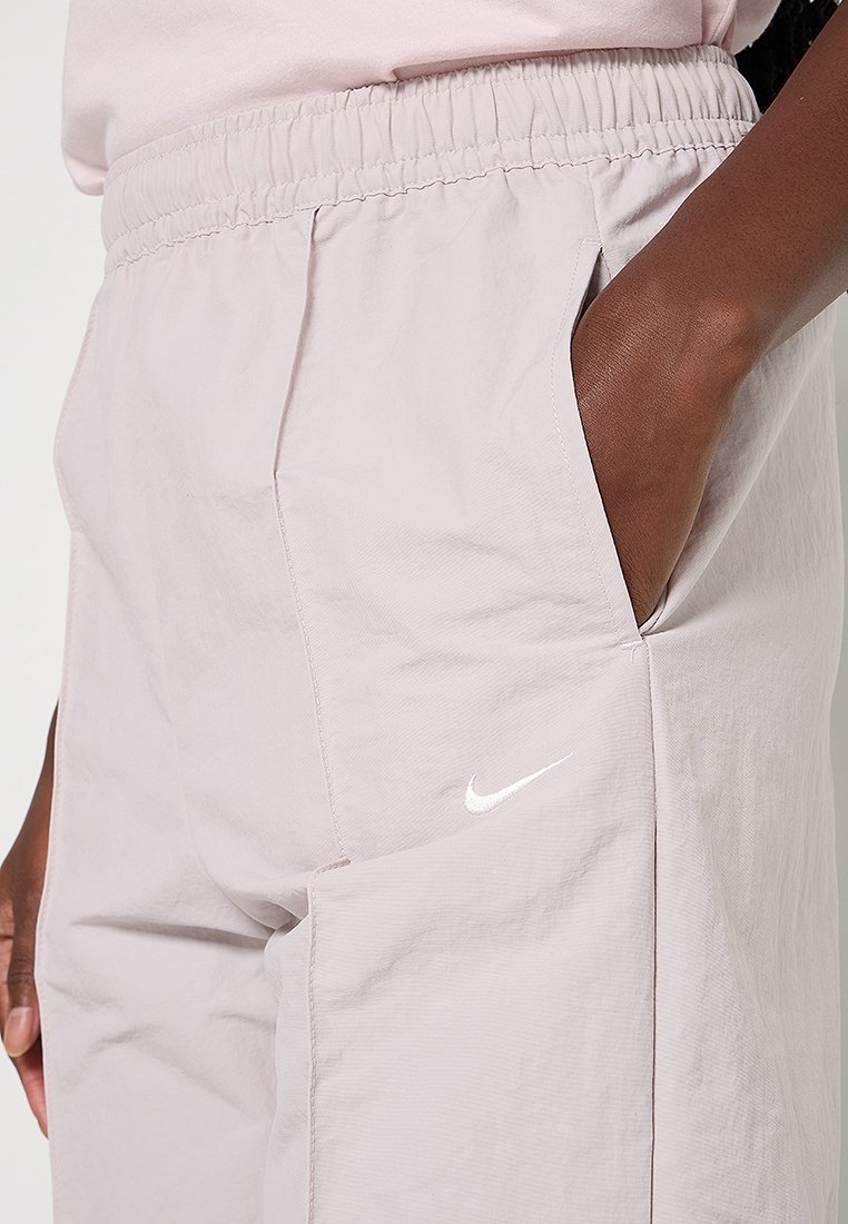 Gros plan d'une personne portant un pantalon Nike rose clair avec une taille élastique et la main dans la poche droite.