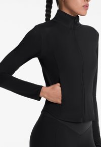 Giacca sportiva nera con colletto alto, maniche lunghe, chiusura a zip e tasca laterale, realizzata in un tessuto liscio e elasticizzato.