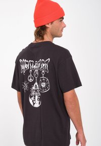 Czarny bawełniany t-shirt z dużą białą grafiką na plecach, przedstawiającą lalkę, zegar i symbol pokoju. Okrągły dekolt i krótkie rękawy.