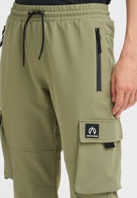 Olive green cargo pants with an elastic waistband, side pockets, and a black patch labeled "NORTH BEND" on the left leg. Textured fabric.