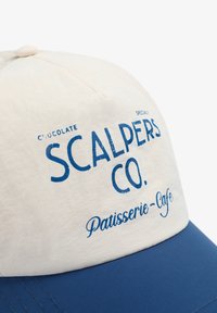Gorra blanca y azul con el texto impreso "SCALPERS CO." y "Patisserie-Café". Tejido suave con un visor estructurado y strap trasero ajustable.