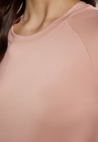 Rosa atletisk top med en glat tekstur, rund halsudskæring og korte ærmer. Har en subtil glans og flade sømme langs kanterne.