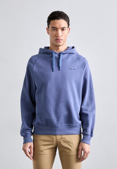 Sweatshirt à capuche bleu en tissu doux, avec une coupe décontractée. Il présente un imprimé de visage souriant et des cordons de serrage contrastants en bleu clair.