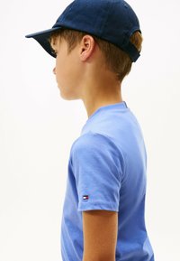 Ragazzo con un cappello blu e una maglietta blu che guarda a sinistra su uno sfondo bianco uniforme.
