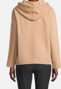 Persikofärgad huvtröja, mjukt tyg, långa ärmar med text på vänster arm, avslappnad passform och en detalj vid bakseam.