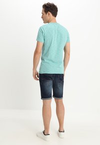Camiseta de algodón de manga corta en color azul claro, combinada con pantalones cortos de mezclilla oscuros, con puños doblados, que cuentan con bolsillos traseros y costuras en contraste.