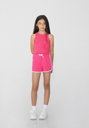 Débardeur côtelé rose vif avec un short assorti et des accents blancs. Baskets et chaussettes blanches. Design simple et sportif, adapté pour l'été.