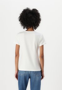 Weißes T-Shirt mit kurzen Ärmeln, rundem Halsausschnitt, glatter Textur und lockerer Passform, kombiniert mit hellblauen Jeans.