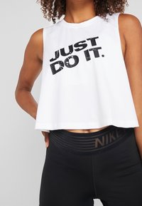 Donna che indossa un top a maniche corte bianco con la scritta "JUST DO IT." e leggings neri a vita alta con il logo Nike sulla cintura.