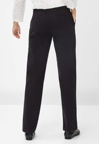 Schwarze, gerade geschnittene Hosen mit Gesäßtaschen, aus einem glatten Stoff gefertigt. Kombiniert mit glänzenden schwarzen Schuhen. Sichtbare Nähte und detailreiche Stickerei.