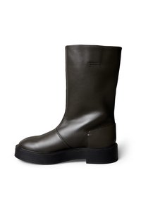 Botín de cuero marrón elegante con acabado suave, puntera redondeada y suela gruesa de goma negra; detalles mínimos de costura visibles.