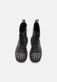 Botas de cuero negro hasta el tobillo con herrajes dorados, diseño de cordones y punta con tachuelas. Presentan una cremallera lateral y suelas texturizadas.