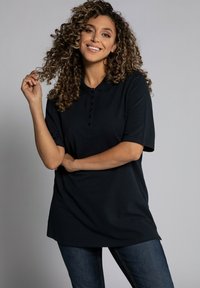 Černé polo tričko s krátkými rukávy, s knoflíkovou légou, uvolněný střih, kombinované s tmavými džíny. Hladká tkanina s klasickým designem límečku.