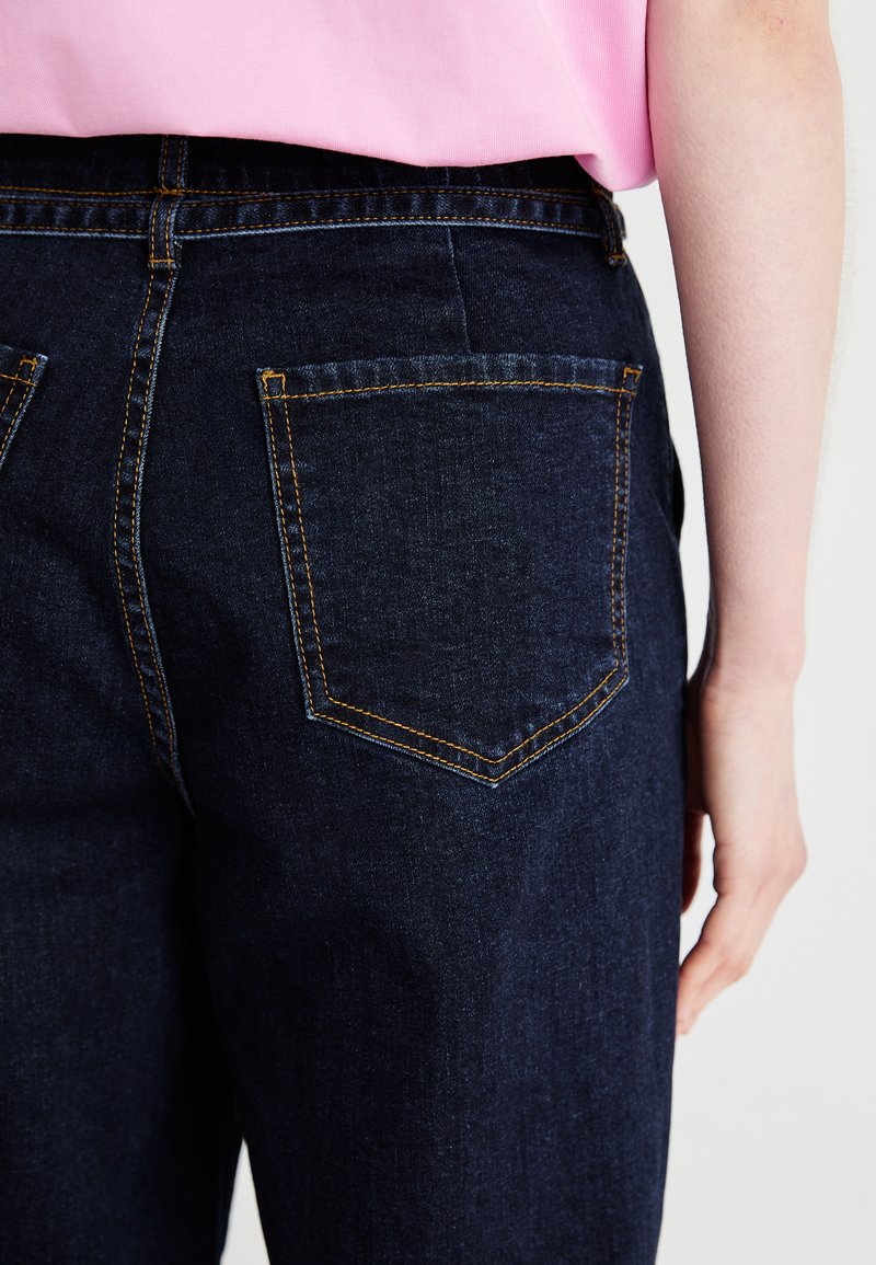 Donkerblauwe denim jeans met een hoge taille, oranje stiksels en twee achterzakken. Glad textuur met een klassiek ontwerp.
