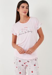Rózsaszín pamut pizsama szett, amely rövid ujjú felsővel rendelkezik, nyuszi grafikával és felirattal, valamint mintás nadrággal, amelyen sütik és nyuszik találhatók.