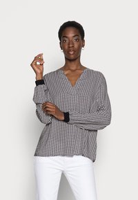 Blusa de manga longa, em V, em malha texturizada preta e branca com detalhes vermelhos, apresentando punhos canelados pretos e um corte descontraído.