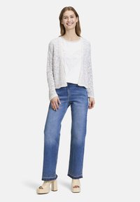 Lättvikts, flerfärgad stickad cardigan över en vit t-shirt med hjärtdesign, parat med blå vida jeans och beige plattformssandaler.