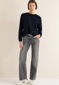Granatowa bluzka z długim rękawem o fakturowanej tkaninie, zestawiona z szerokimi dżinsami w jasnoszarym kolorze oraz białymi trampkami z kolorowymi akcentami.