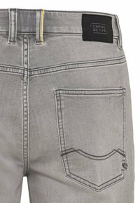 Graue Denim-Hosen zeigen eine Nahaufnahme der Gesäßtasche, mit kontrastierenden Nähten und einem markierten dunklen Etikett am Bund.