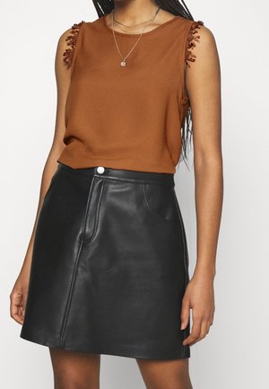 Ærmeløs brun top med blonder detaljer på skuldrene, kombineret med sort læder A-formet nederdel med høj talje og lagdelte sølvsmykker.