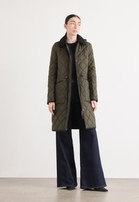 Gevoerde olijfgroene parka met een zwarte kraag, ritssluiting en drukknoopsluitingen, twee voorzakken en zwarte accenten; getailleerde pasvorm, knielengte.