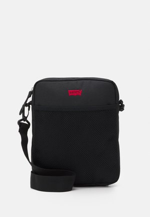 Bolsa mensajera negra con un panel de malla texturizada, correa ajustable y logo rojo. Diseño compacto, cierre de cremallera y material ligero.