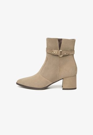 Stivaletto in suede taupe con punta affusolata, zip laterale e una fascia decorativa con fibbia. Tacco a blocco per stabilità e una texture liscia.