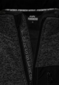 Grauer Pullover mit hohem Kragen und Reißverschluss. Der Markenname "FORSBERG" ist in einer kontrastierenden Farbe entlang des Reißverschlusses gestickt.