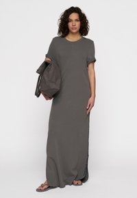 Robe grise, mi-longue, à manches courtes, en tissu doux avec une coupe décontractée, des fentes sur les côtés et un décolleté rond. Associée à un sac gris.