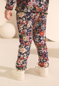 Blå byxor med blommönster och ribbad struktur. Volangkant vid fållen, kombinerat med vita sneakers. Ljusa, flerfärgade blommönster.