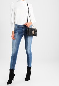 Biała bluzka z długim rękawem z wytłaczanym detalem, zestawiona z niebieskimi obcisłymi jeansami i czarnymi botkami na szpilce. Czarna torebka z srebrnymi okuciami.
