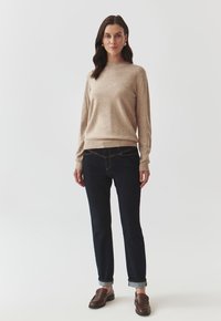 Pulover bej cu mâneci lungi, blugi închisi cu manșete răsucite, mocasini maro; textură fină din lână, croială casual, design minimalist.