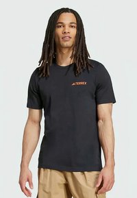 Juodas trumpas rankovėmis marškinėliai iš minkštos medžiagos, su oranžiniu "TERREX" logotipu ant krūtinės, tradicinio apvalaus kaklo dizainas.