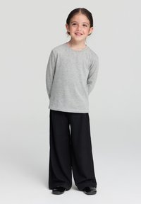 Maglietta a maniche lunghe grigia abbinata a pantaloni neri a gamba larga e a coste, caratterizzati da una vestibilità rilassata e un design minimalista. Scarpe nere slip-on.